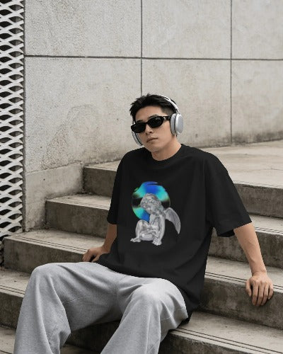 Person wearing a black t-shirt with a graphic design, sitting on steps against a concrete wall.